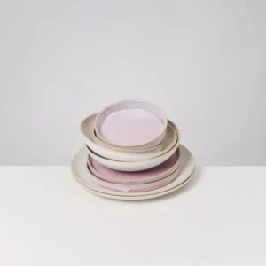 Ein Stapel Keramikteller und -schalen mit rosa Glasur steht auf einem weißen Tisch.